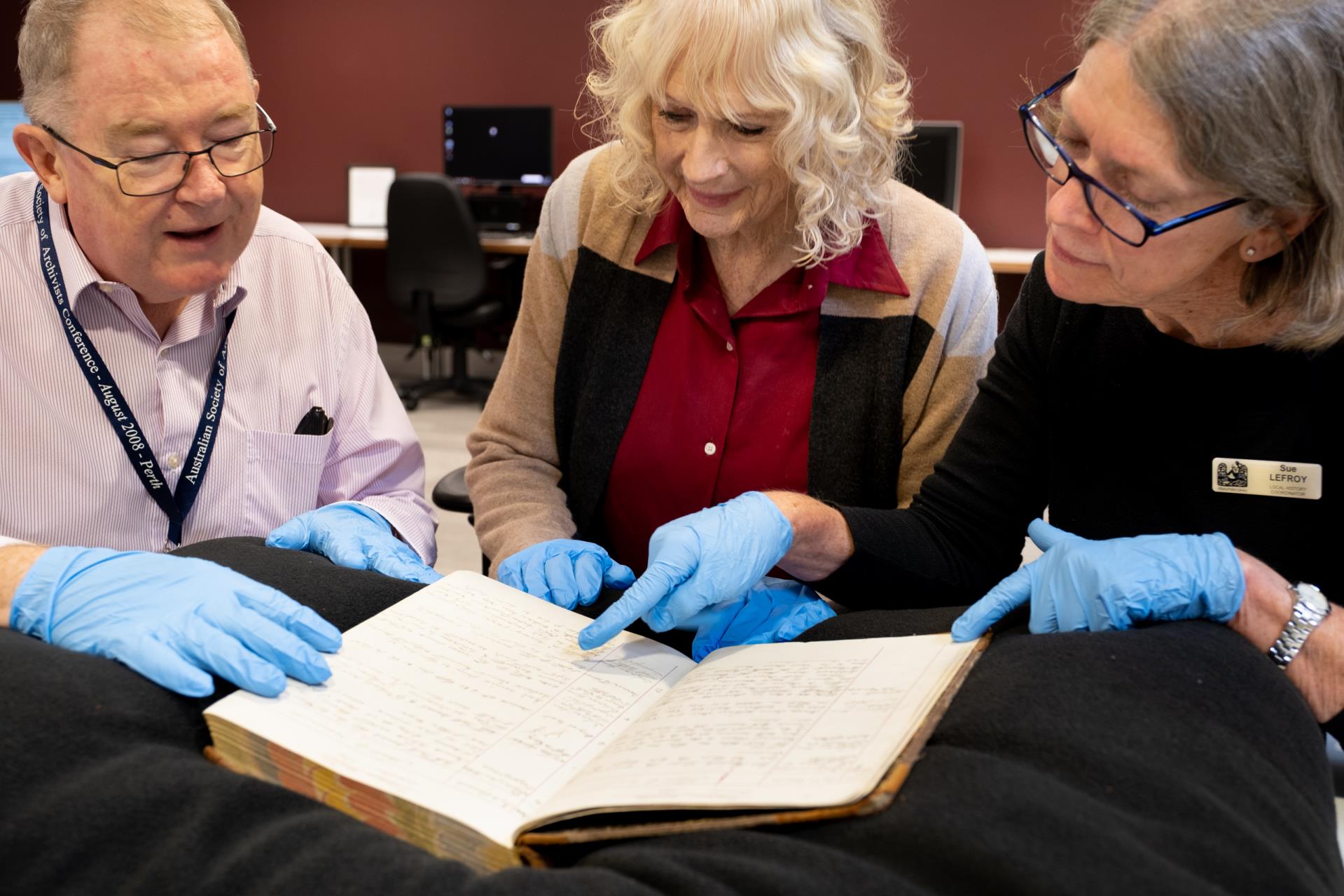 Sue Lefroy with State Library Office staff inspecting at Williams Police Occurrence Book from 1879-1881