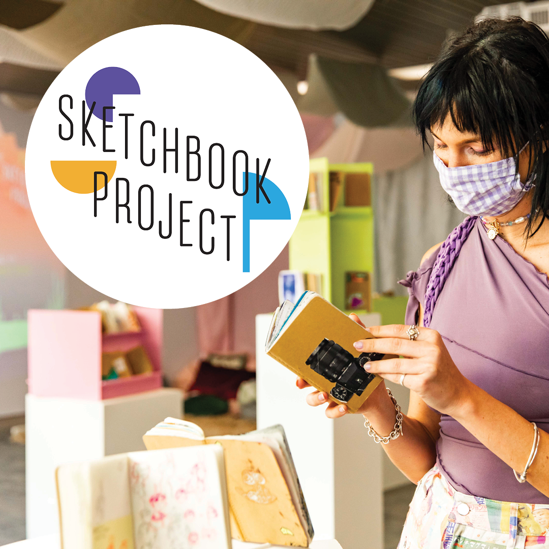 Woman wearing a face mask browses a sketchbook in front of a library display